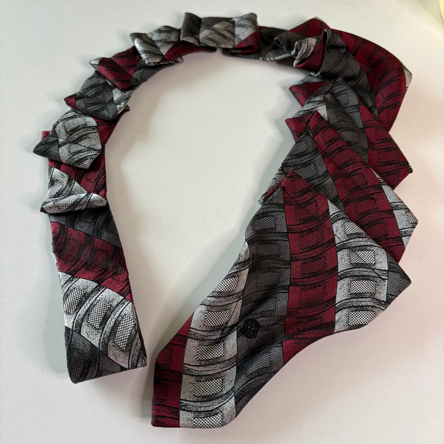 Red, gray, and black patterned tie with snap fastener on a mannequin head.