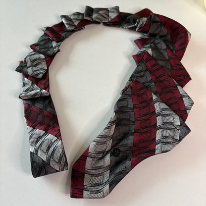 Red, gray, and black patterned tie with snap fastener on a mannequin head.