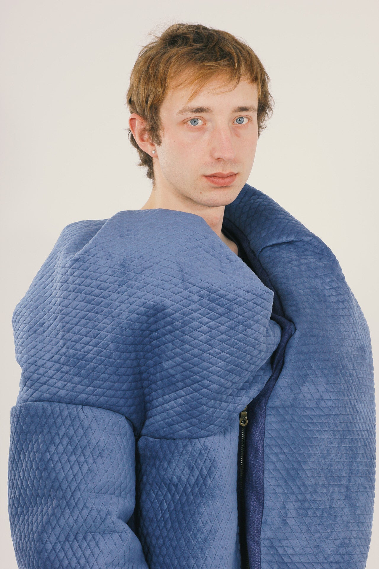 Person wearing a large blue quilted jacket against a plain background