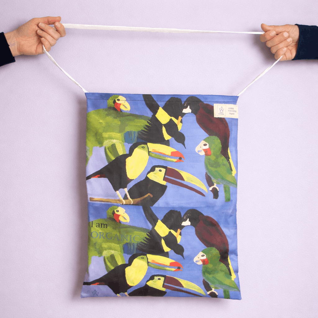 Tote Bag with colorful parrot design held by two hands against a light purple background