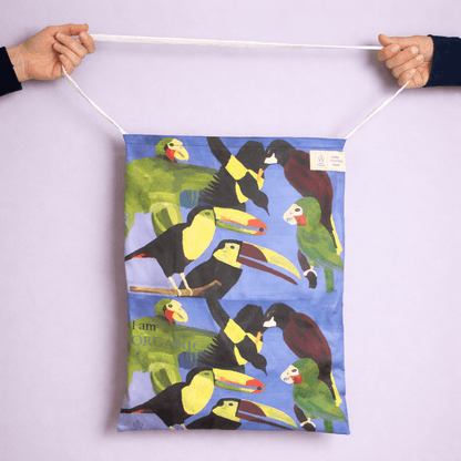 Tote Bag with colorful parrot design held by two hands against a light purple background