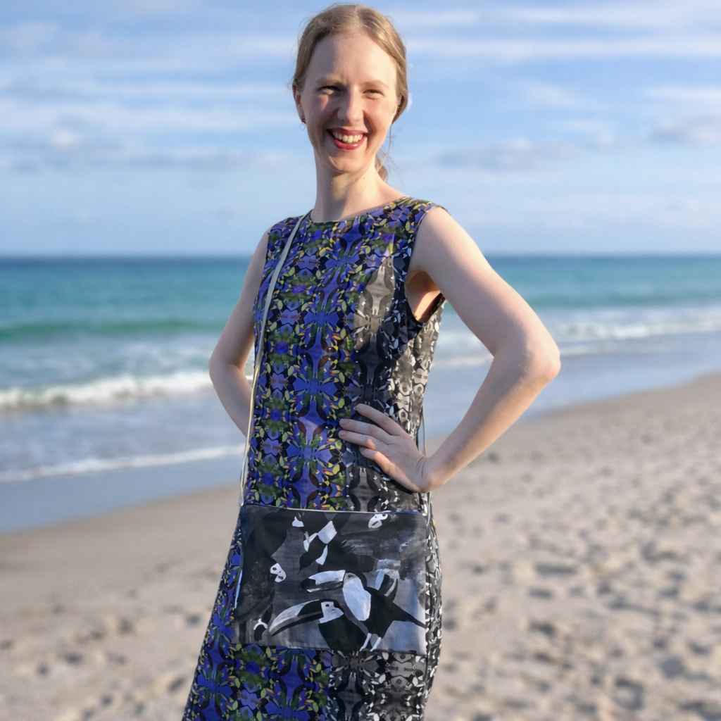 Woman standing on a beach wearing a floral dress with a black and white patterned bird bag.