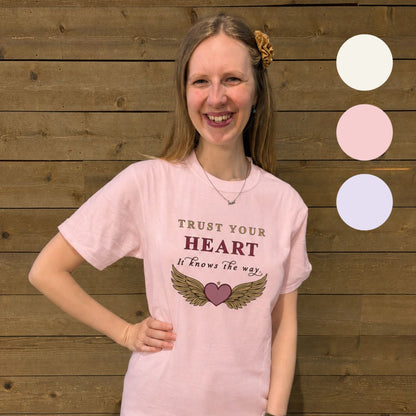 Person wearing a pink t-shirt with a motivational quote and design, standing against a wooden background.