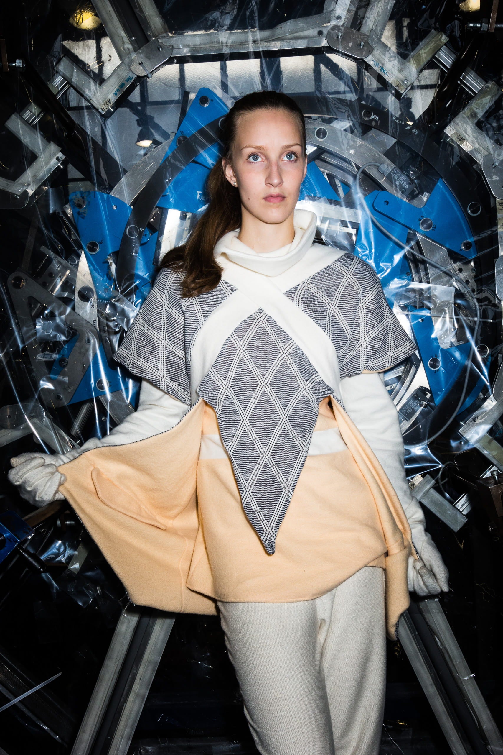 Woman wearing a blue and white dress over a beige outfit in front of a reflective, abstract background.