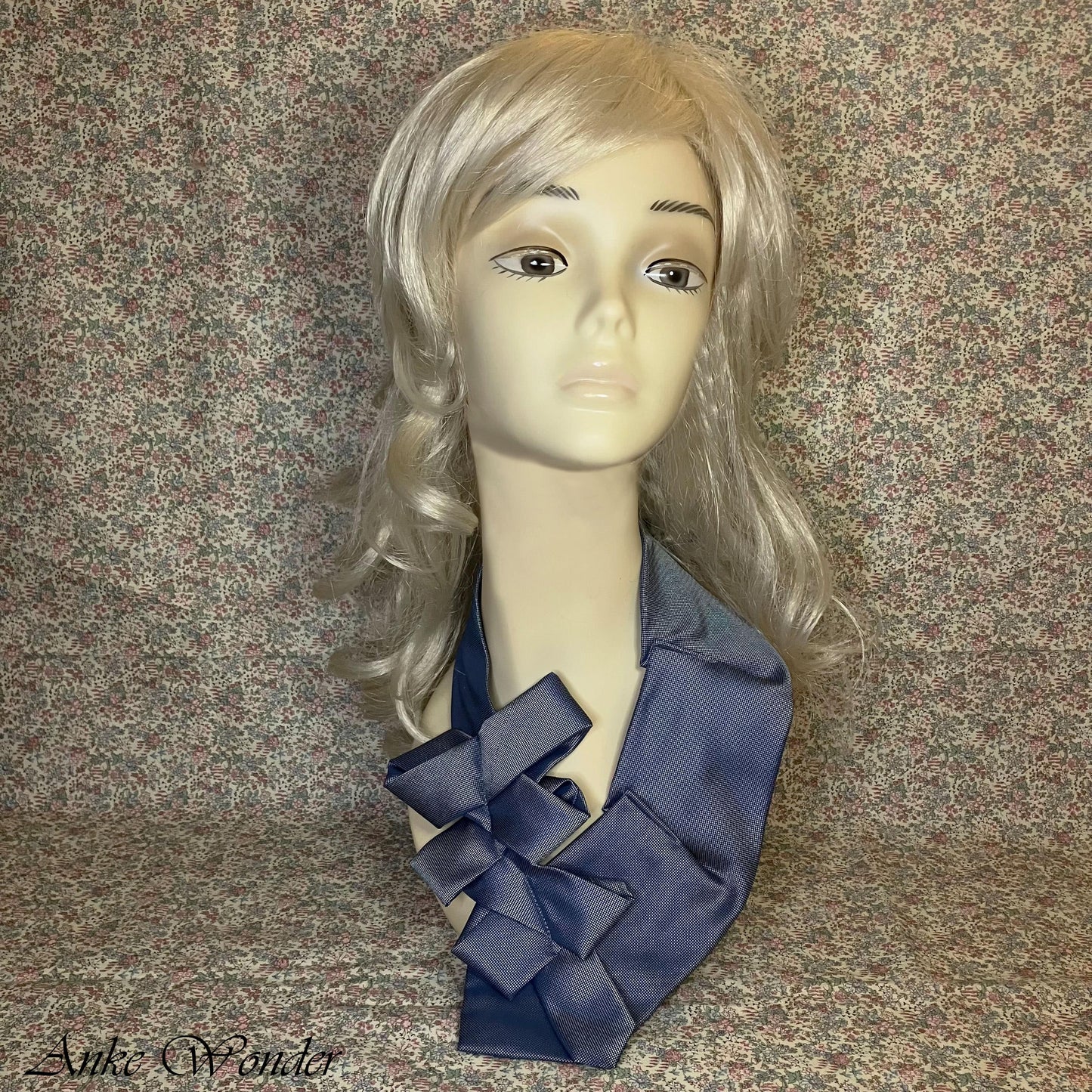 Full front view of a blue women's necktie displayed on a mannequin, featuring a bold bow-like layered design and a subtle sheen on the fabric.