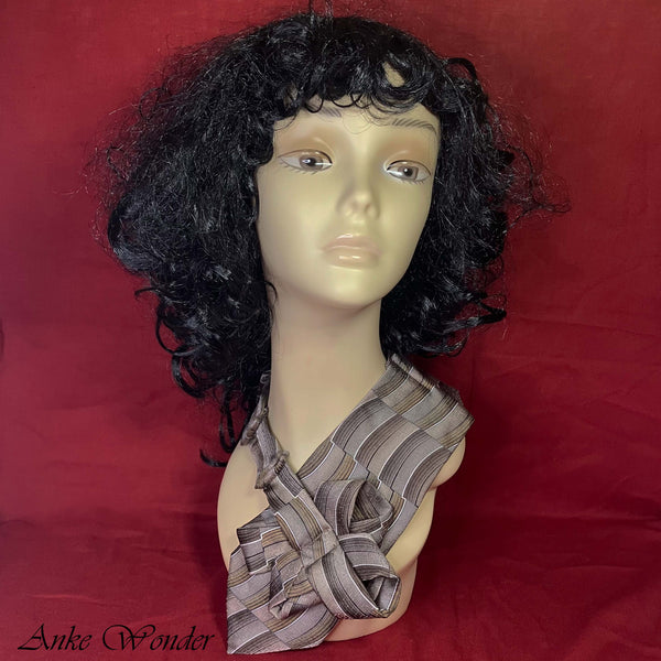 Mannequin wearing a handmade women's gray silk necktie with a pleated, upcycled striped design against a red background.