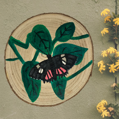 Hand-painted wooden slice featuring a vibrant red postman butterfly against a green wall. The rustic wooden art piece showcases intricate details of the butterfly, highlighting its natural charm.
