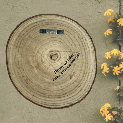 Back view of the wooden slice with mounting apparatus displayed against a green wall. Ready-to-hang artwork with a simple and sturdy setup.