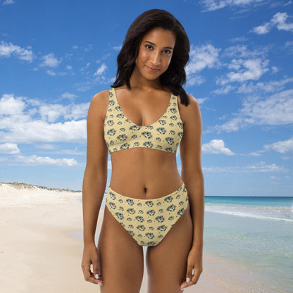 Woman in a floral sunflower bikini standing on a beach with blue sky and ocean in the background.