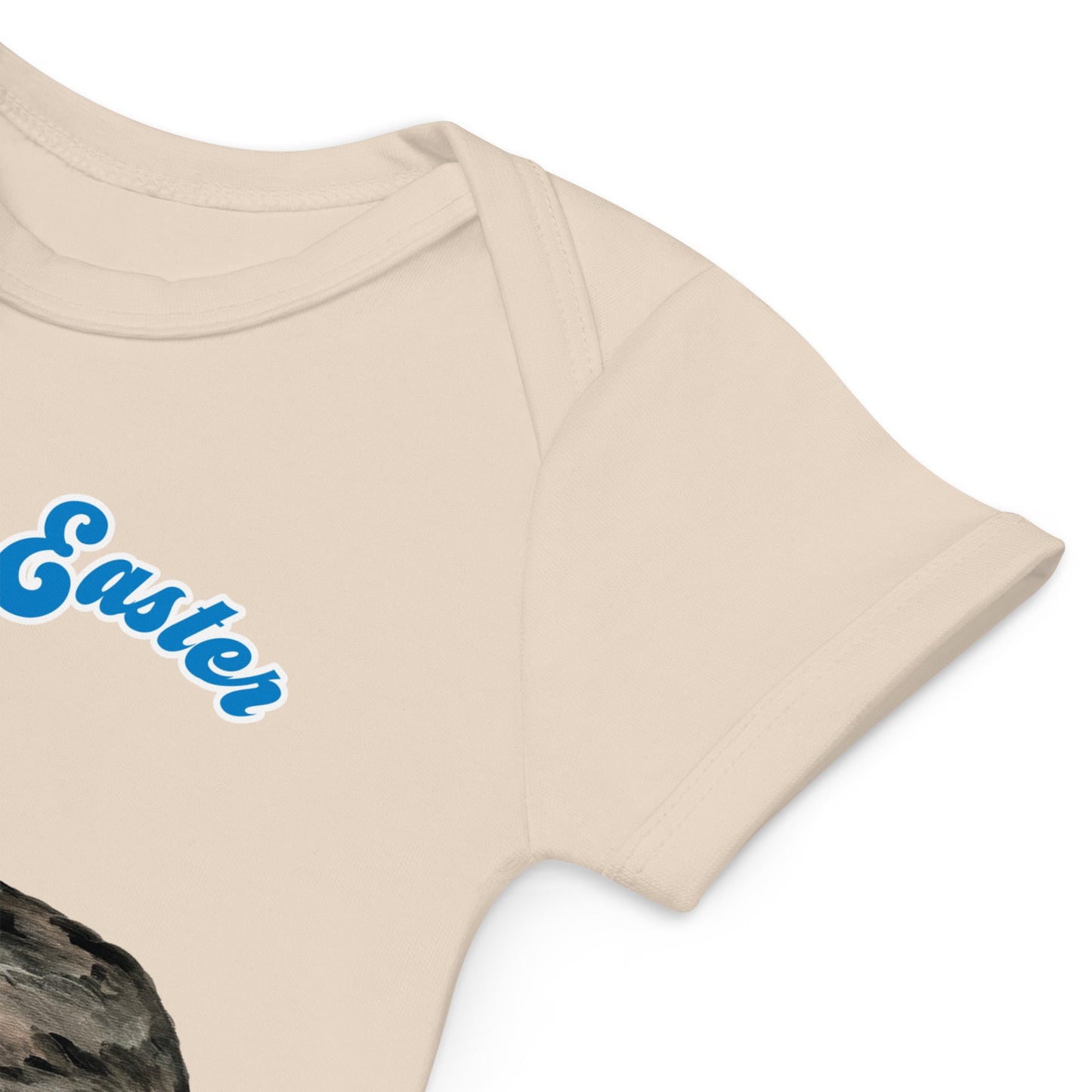 Close-up view of envelope sleeve of a natural color short-sleeve organic cotton baby bodysuit featuring a bunny and Easter basket design, with 'My First Easter' in blue text.
