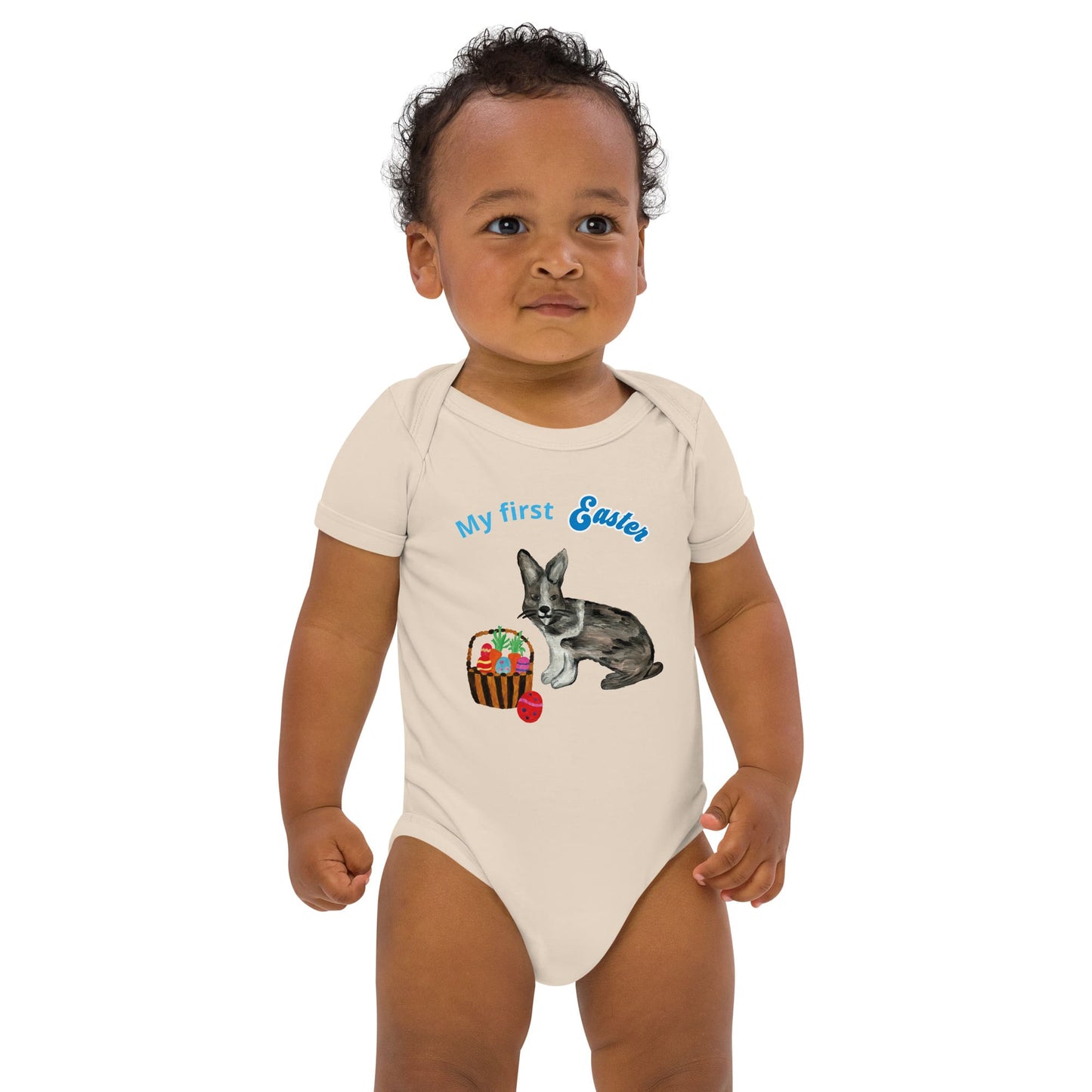 A baby boy wearing anatural color short-sleeve organic cotton bodysuit with a bunny and Easter basket graphic, plus the text 'My First Easter' in blue.