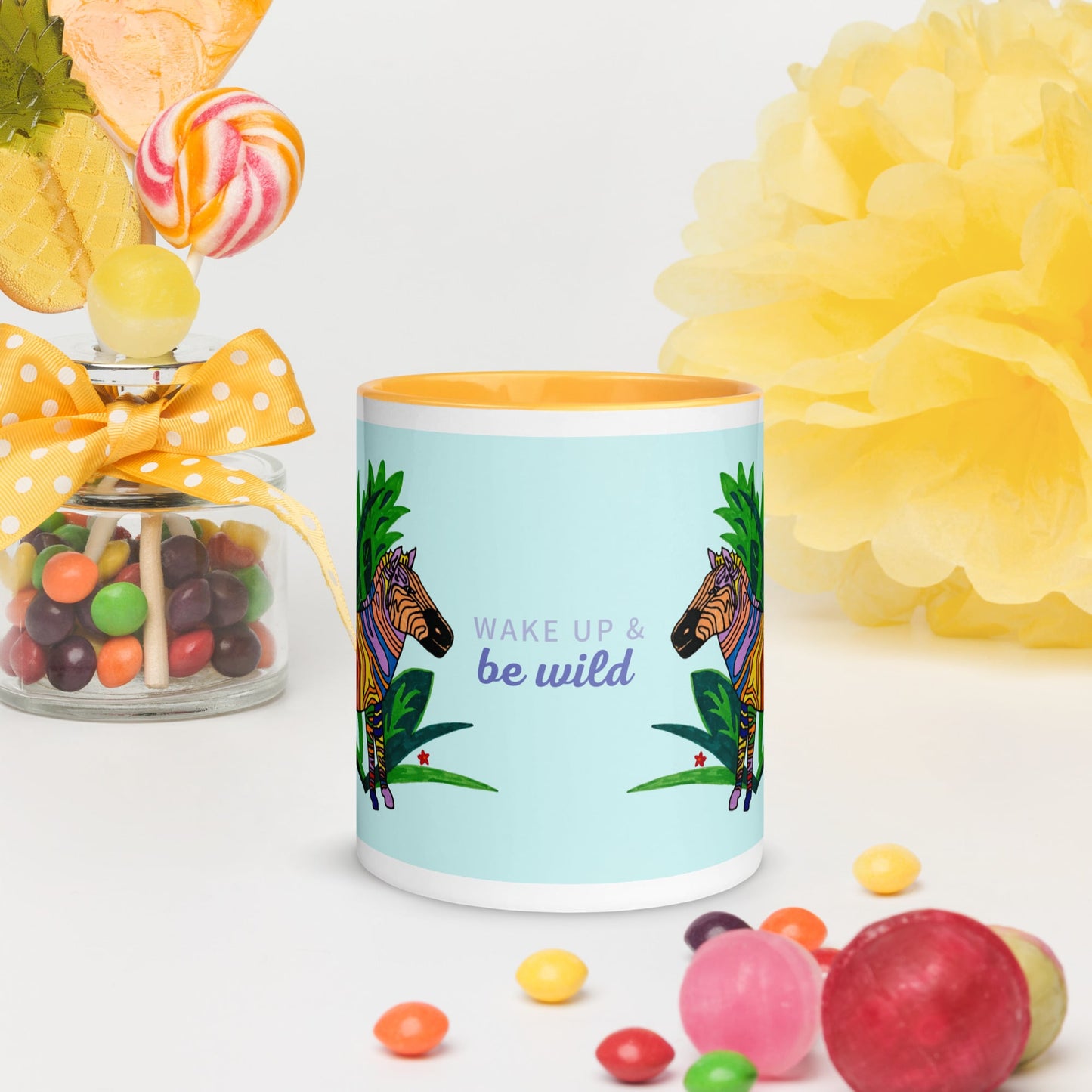 Ceramic mug with zebra design and 'Wake up & be wild' text, surrounded by colorful candies and flowers.