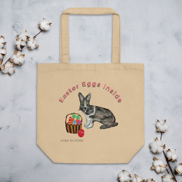 Beige organic cotton tote bag with "Easter Eggs Inside" text and a watercolor illustration of a bunny and Easter egg basket by ANKE WONDER.