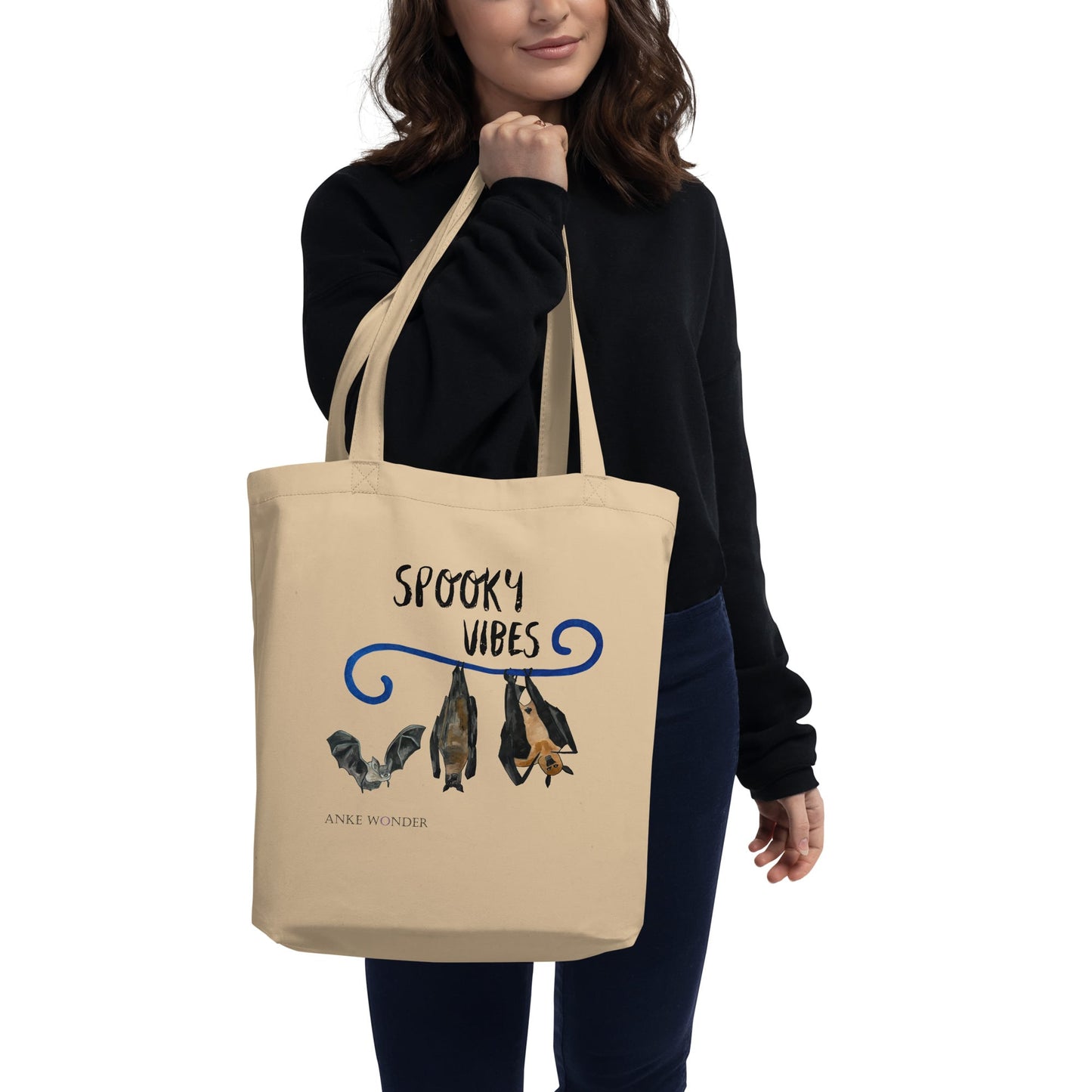 Person holding a beige tote bag with 'Spooky Vibes' text and bat design on a white background