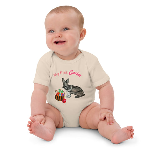 A baby girl wearing a short-sleeve organic cotton bodysuit with pink 'My First Easter' text, featuring a bunny and basket design.