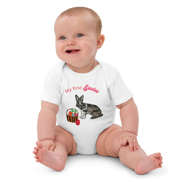 A baby girl wearing a short-sleeve organic cotton white bodysuit with pink 'My First Easter' text, featuring a bunny and basket design.