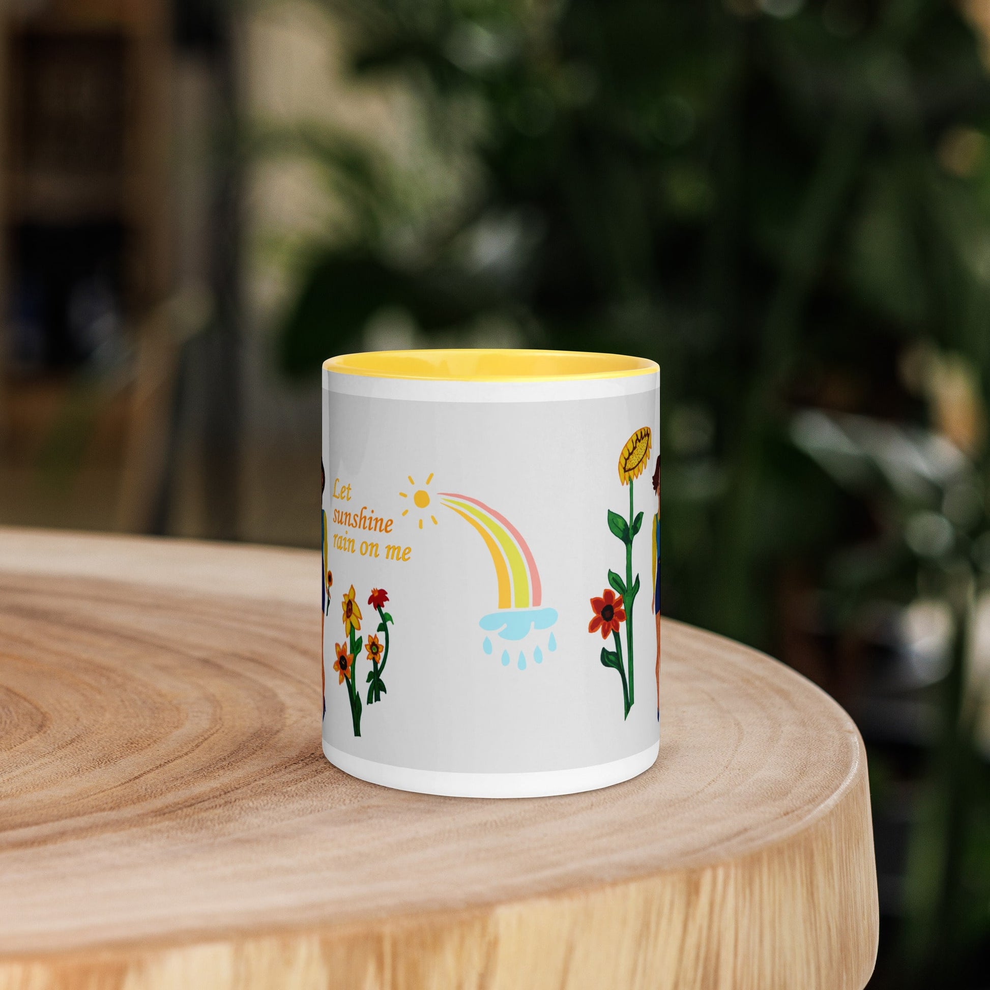 White mug with colorful designs and text 'Let sunshine rain on me' on a wooden surface