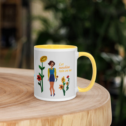 Mug with a design of a woman, sunflowers, and text 'Let sunshine run on me' on a wooden surface.