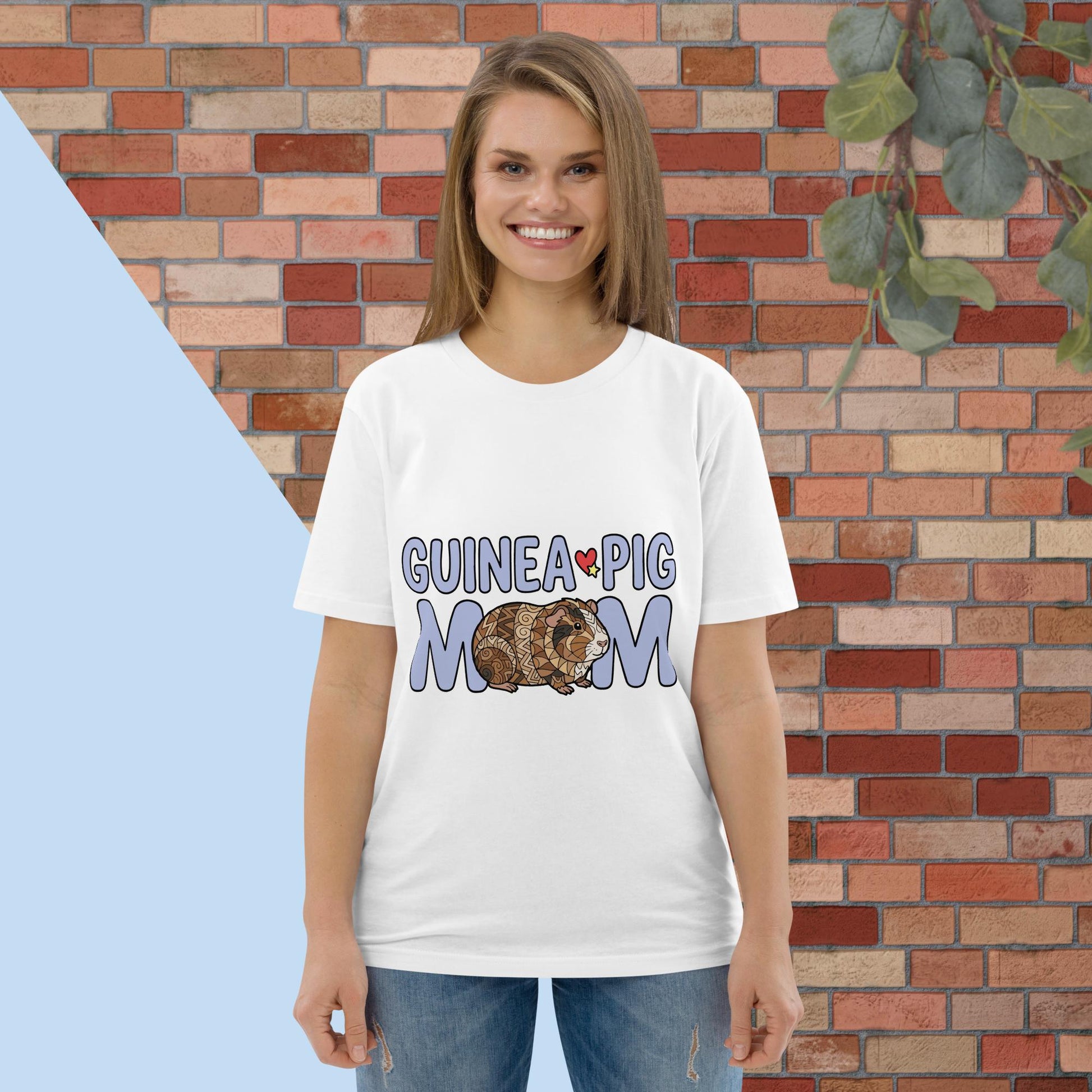 Woman wearing a white t-shirt with 'Guinea Pig Mom' design against a brick wall.