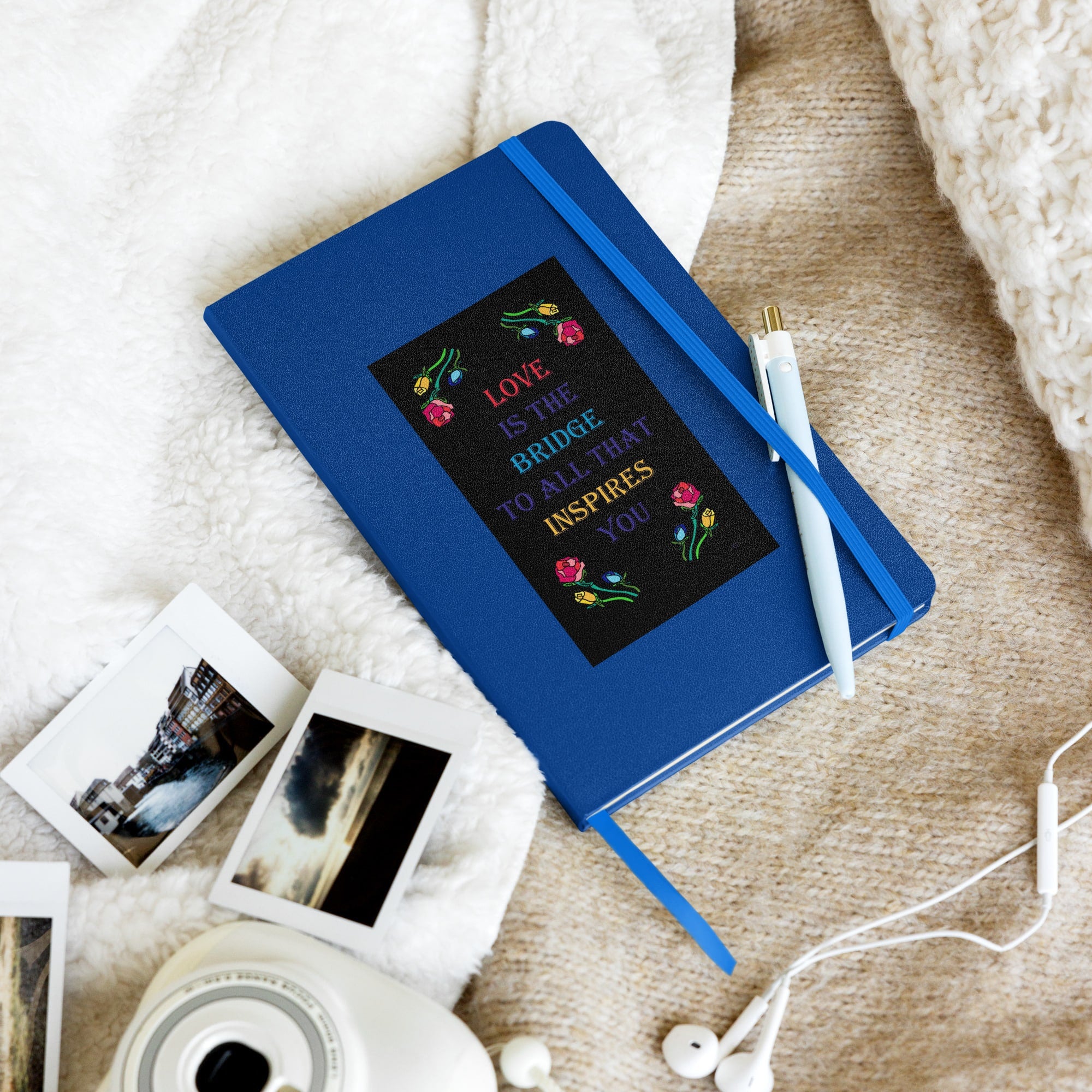 Hardcover notebook with blue binding featuring the quote "Love is the bridge to all that inspires you" in colorful text with floral designs.