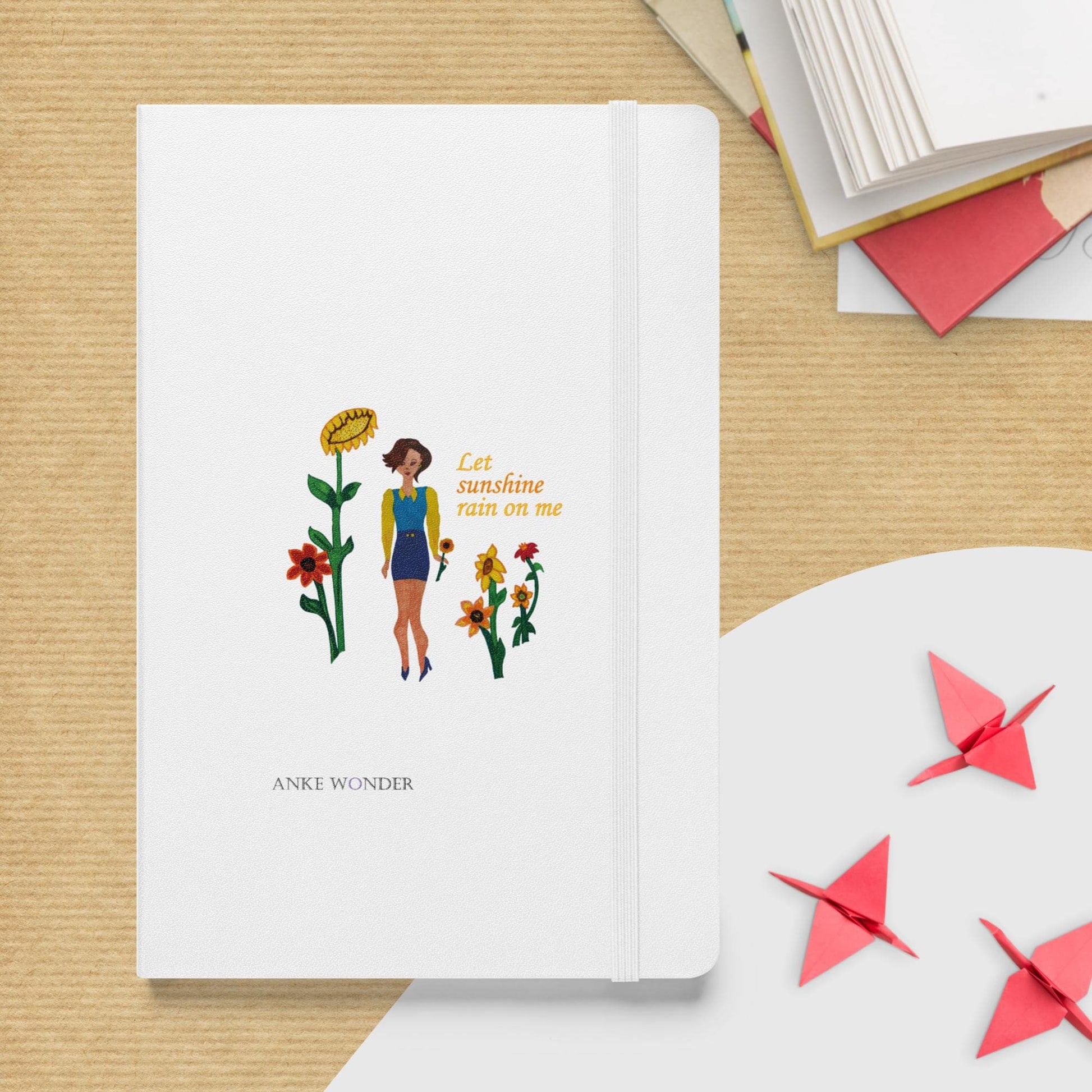 Notebook with illustration of a woman and flowers on a wooden surface with origami cranes.