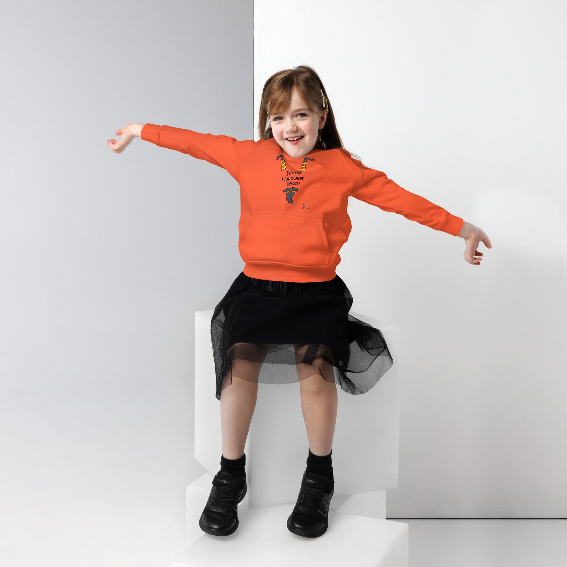 Child wearing an orange hoodie with Halloween design and black skirt on a white background