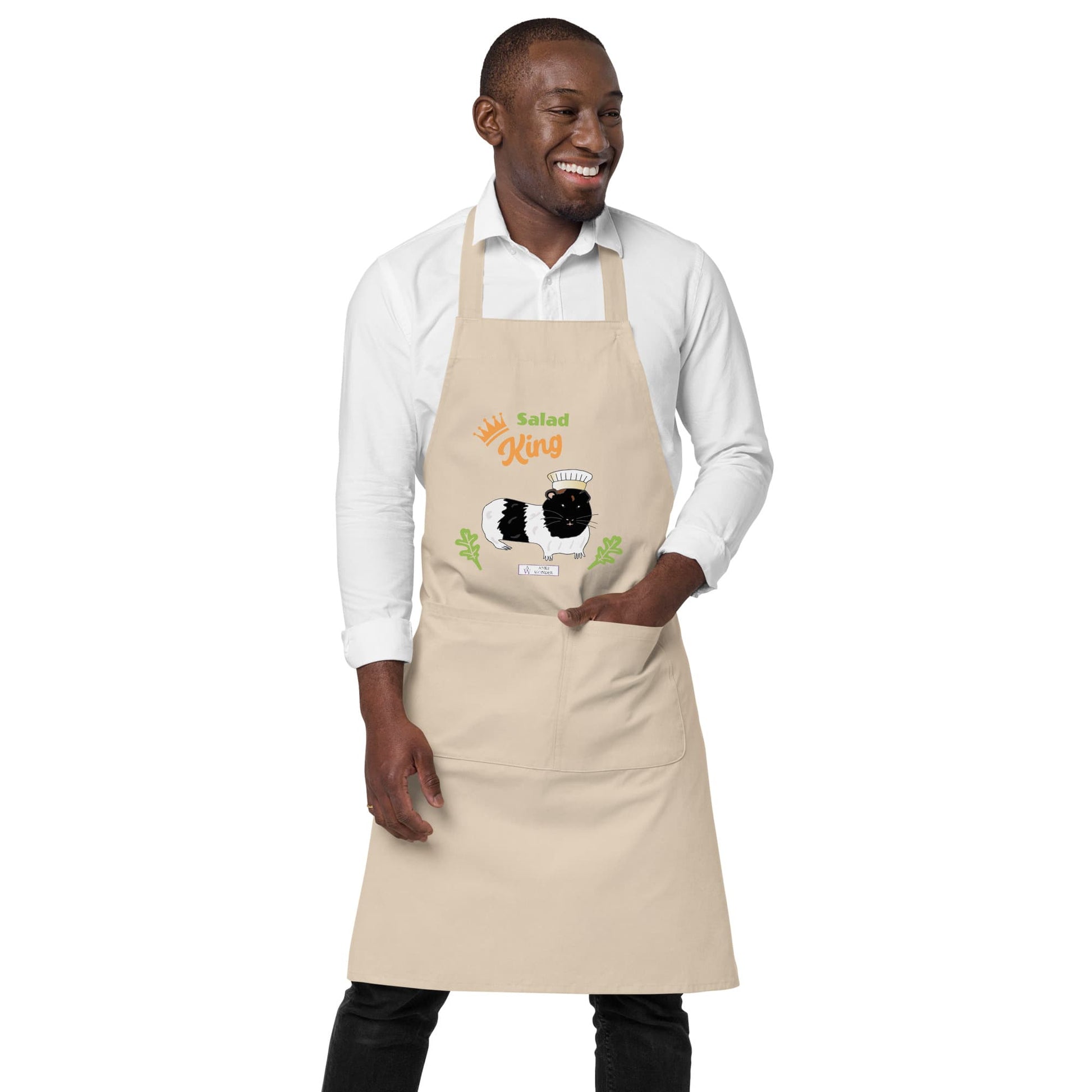 A man wears a beige apron featuring a guinea pig chef design and the words 'Salad King' in green and orange.