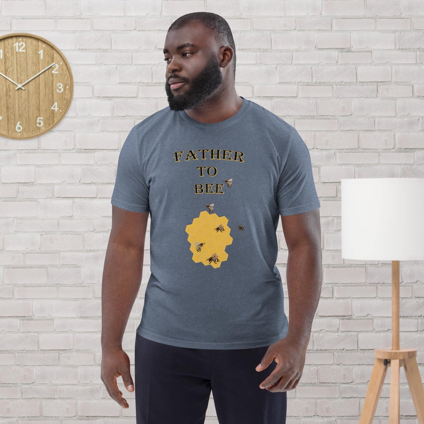 Man wearing a dark heather blue organic cotton t-shirt with “Father to Bee” text and bee graphic, standing in a modern room.