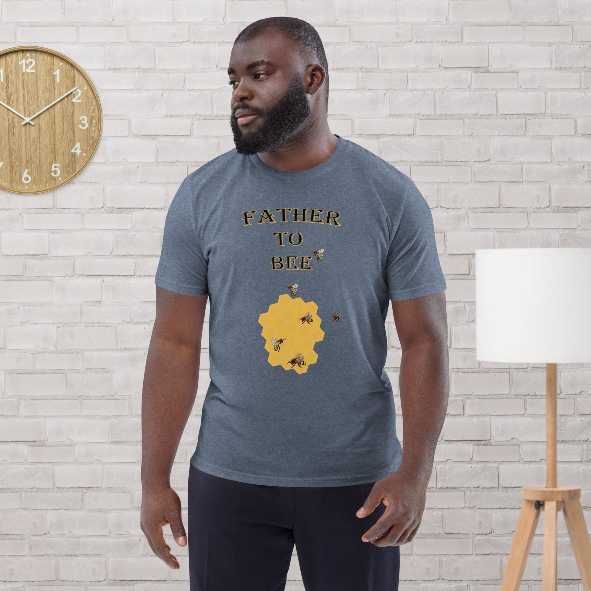 Man wearing a dark heather blue organic cotton t-shirt with “Father to Bee” text and bee graphic, standing in a modern room.