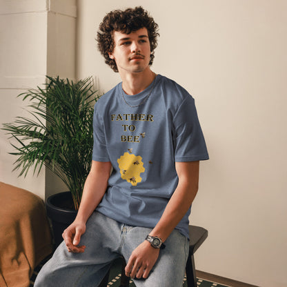 Man wearing a dark heather blue “Father to Bee” organic cotton t-shirt at a slight front angle, standing in a cozy room setting.