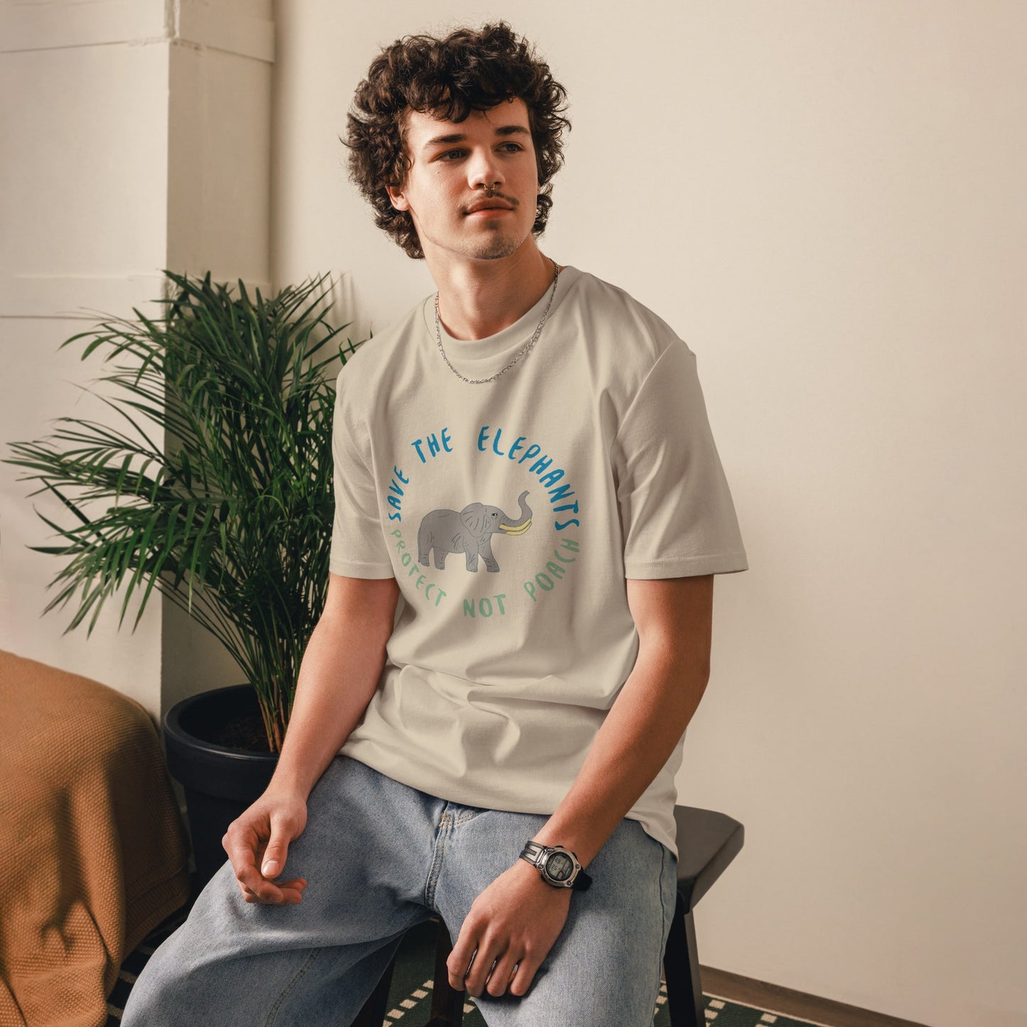 Man sitting while wearing a lavender “Save the Elephants – Protect Not Poach” organic cotton t-shirt; the relaxed posture and minimalist setting highlight the soft, ethical fabric.
