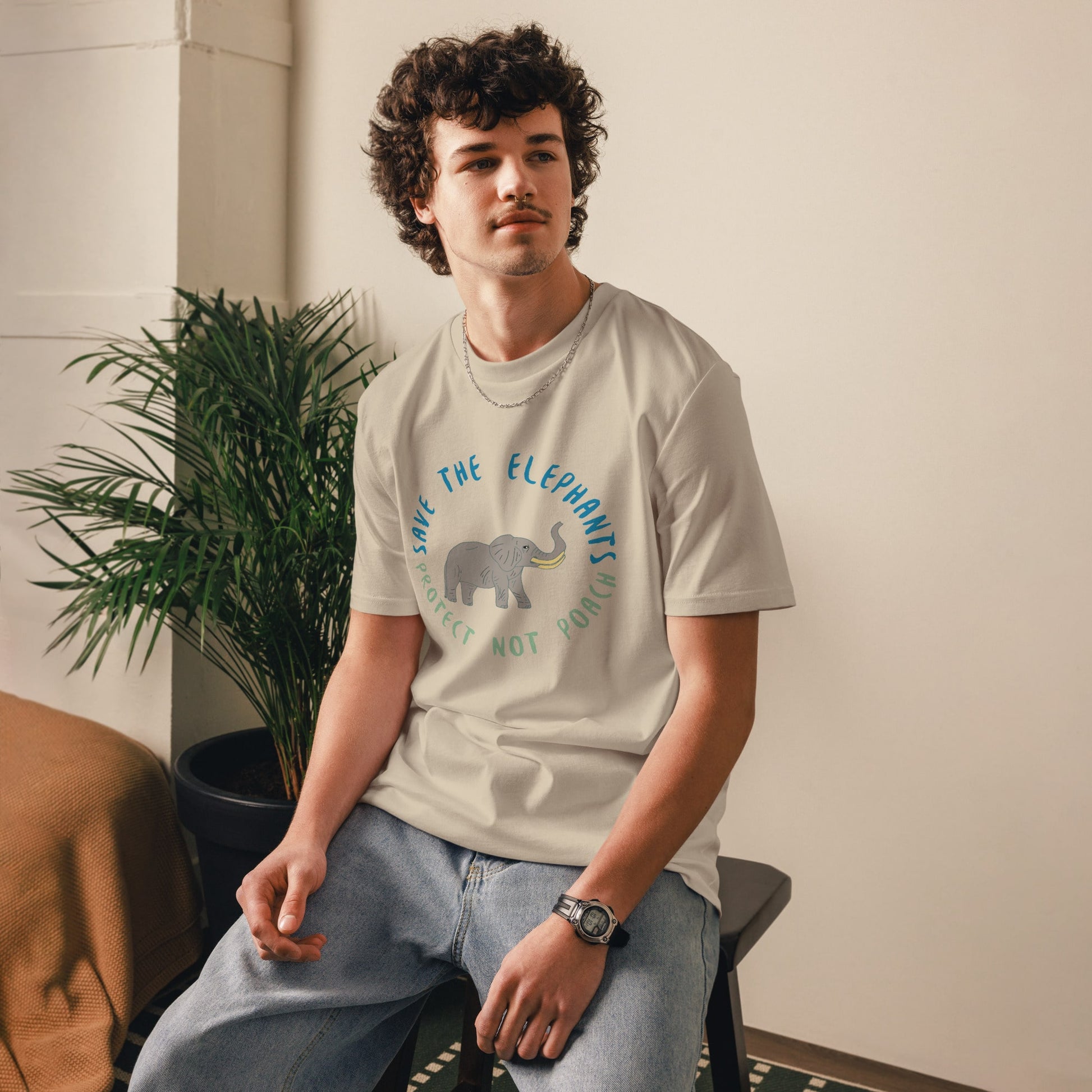 Man sitting while wearing a lavender “Save the Elephants – Protect Not Poach” organic cotton t-shirt; the relaxed posture and minimalist setting highlight the soft, ethical fabric.