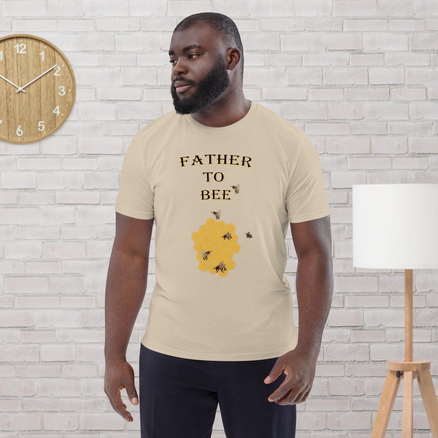 Man wearing a desert dust organic cotton t-shirt with “Father to Bee” text and bee graphic, standing in a modern room.