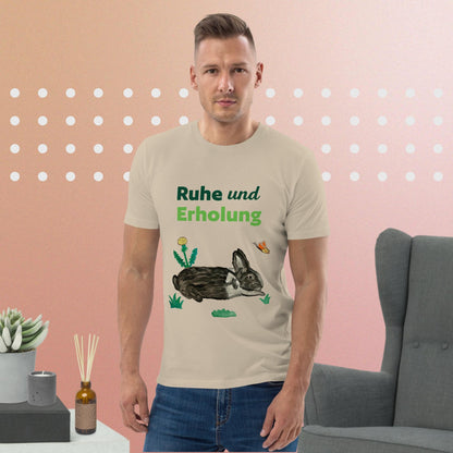 Man wearing desert dust organic cotton t-shirt featuring hand-painted black-and-white rabbit with butterfly and greens, and the words "Ruhe & Erholung" on the front.