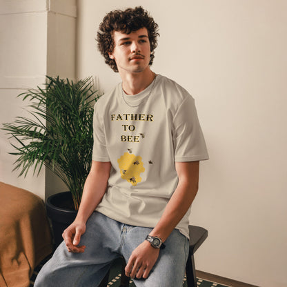 Man wearing a desert dust “Father to Bee” organic cotton t-shirt at a slight front angle, standing in a cozy room setting.