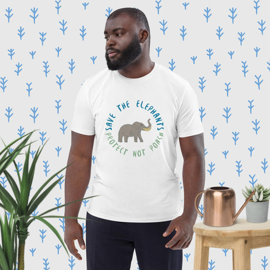 Man wearing a white organic cotton t-shirt with a hand-illustrated elephant and the message “Save the Elephants – Protect Not Poach”; front view, right angle. He stands in a minimal indoor setting with botanical accents, evoking a calm, nature-inspired mood.