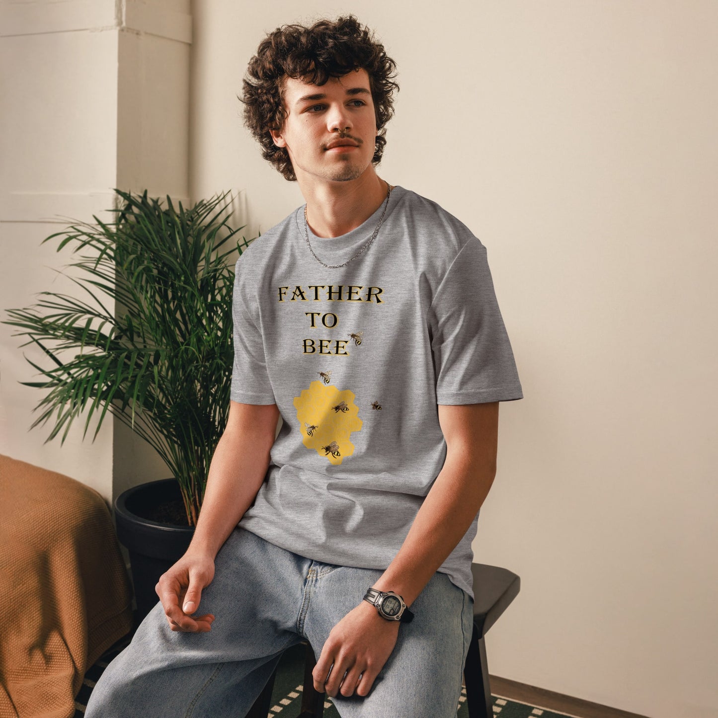 Man wearing a heather grey “Father to Bee” organic cotton t-shirt at a slight front angle, standing in a cozy room setting.