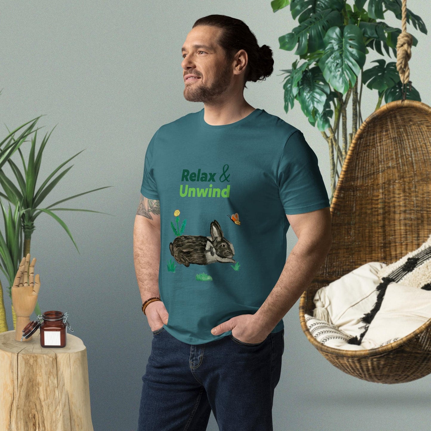 Man wearing deep blue organic cotton t-shirt with hand-painted black-and-white rabbit, greens, butterfly, and "Relax & Unwind" text — front view, right angle.