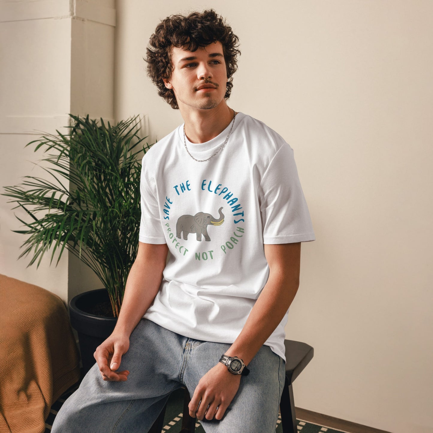 Man sitting while wearing a white “Save the Elephants – Protect Not Poach” organic cotton t-shirt; the relaxed posture and minimalist setting highlight the soft, ethical fabric.