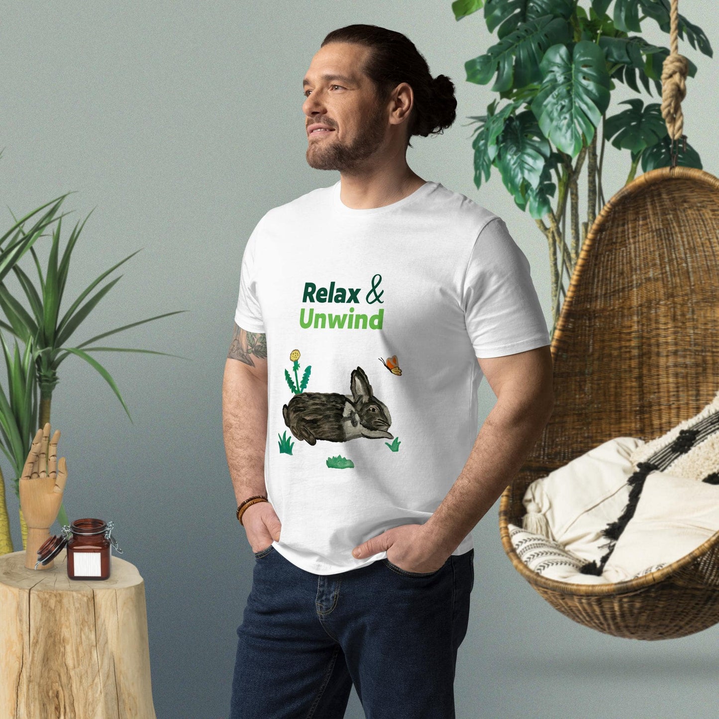Man wearing white organic cotton t-shirt with hand-painted black-and-white rabbit, greens, butterfly, and "Relax & Unwind" text — front view, right angle.