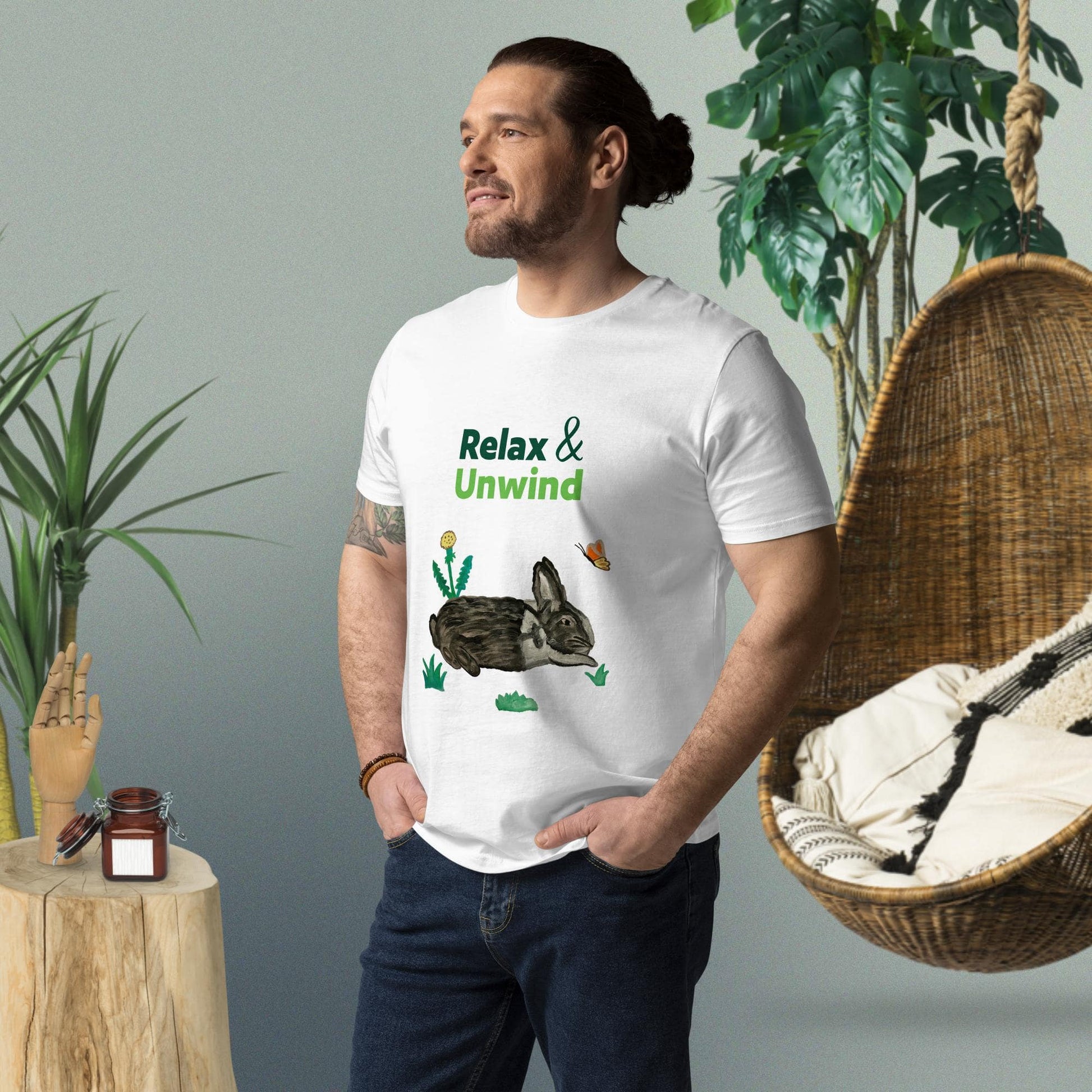 Man wearing white organic cotton t-shirt with hand-painted black-and-white rabbit, greens, butterfly, and "Relax & Unwind" text — front view, right angle.