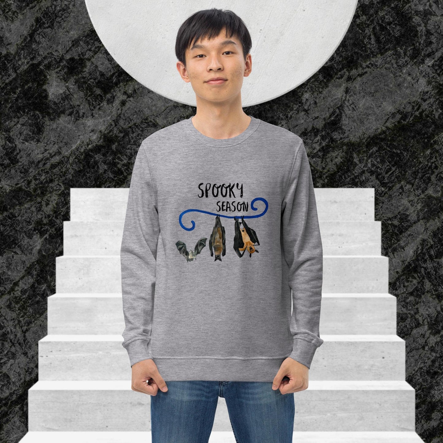 Man wearing a gray sweatshirt with 'Spooky Season' design and bat illustration on stairs