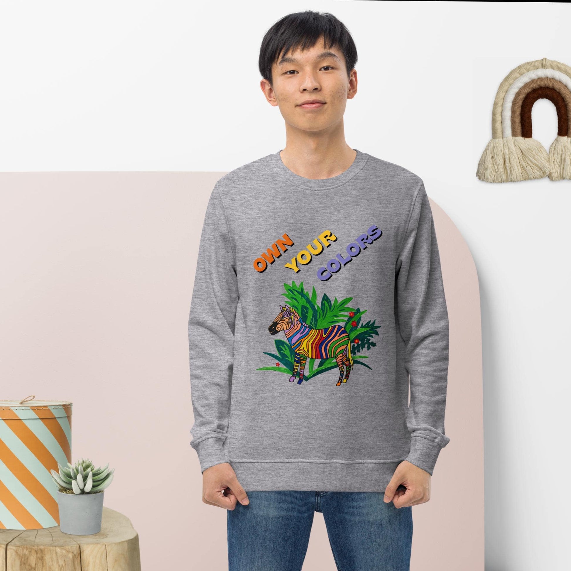 Man wearing a gray sweatshirt with colorful text and animal design, standing against a light pink wall.