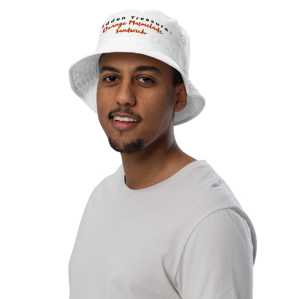 Model wearing a white bucket hat with "Hidden Treasure: Orange Marmalade Sandwich" embroidery on the front, adding a playful touch to their outfit.