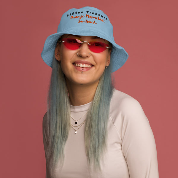 Model wearing a blue bucket hat with "Hidden Treasure: Orange Marmalade Sandwich" embroidery on the front, adding a playful touch to their outfit.