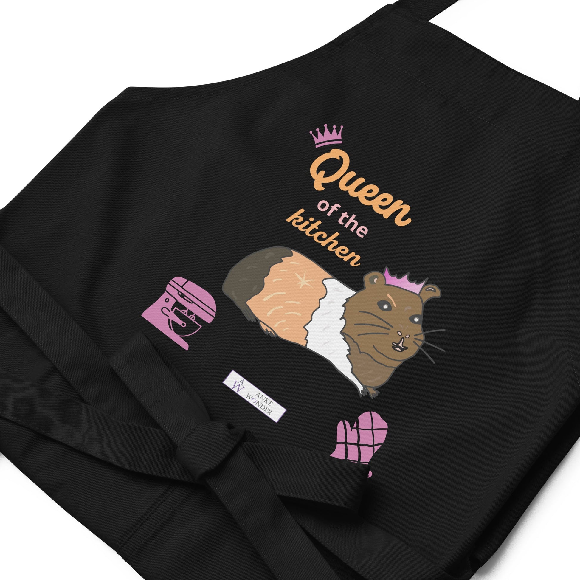 A flat-lay of the navy apron displaying the guinea pig in a pink crown and bold “Queen of the Kitchen” text with the Anke Wonder branding.