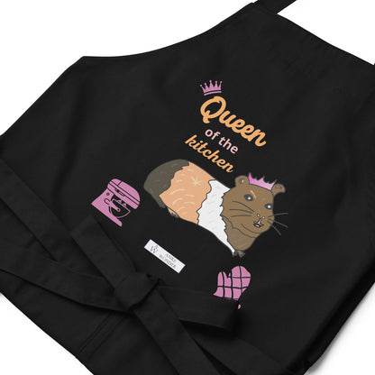 A flat-lay of the navy apron displaying the guinea pig in a pink crown and bold “Queen of the Kitchen” text with the Anke Wonder branding.