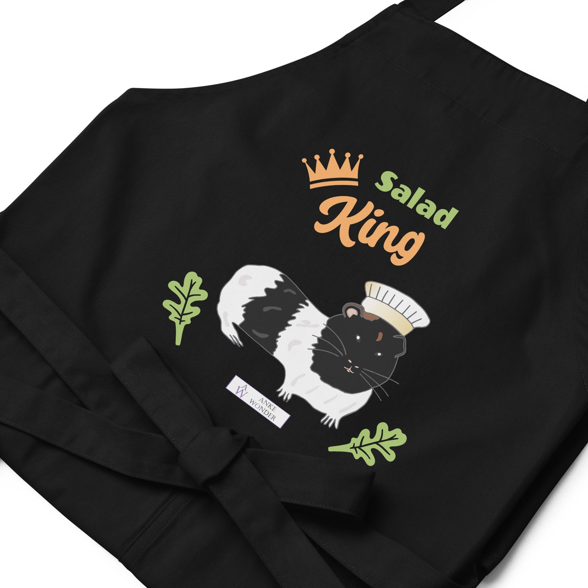A flat-lay of the black Salad King apron, showing the detailed guinea pig illustration and the Anke Wonder Logo.