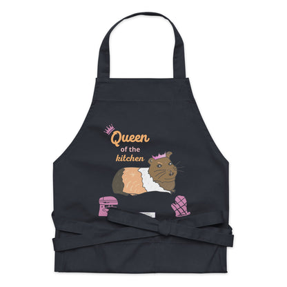 A flat-lay of the navy apron displaying the guinea pig in a pink crown and bold “Queen of the Kitchen” text.