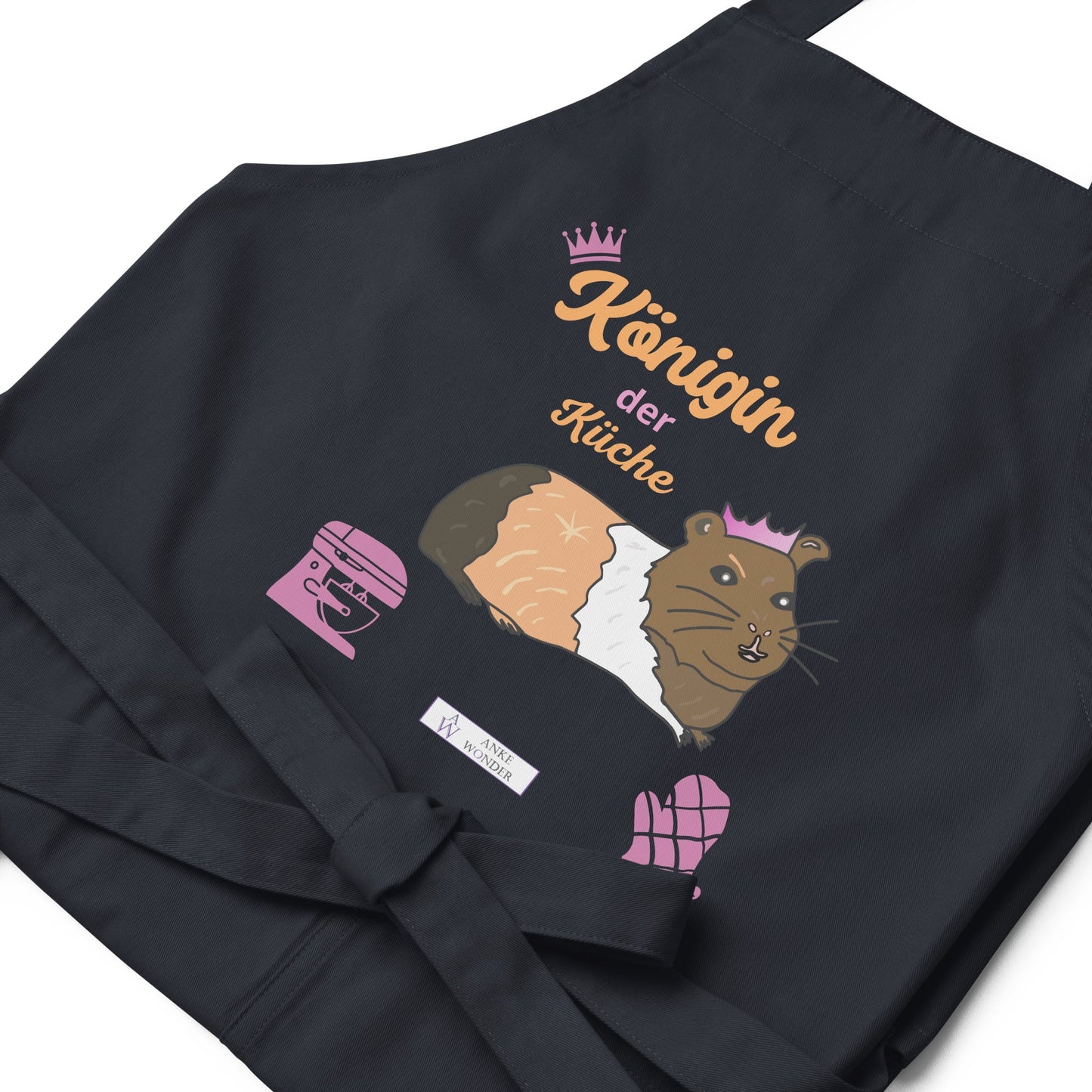 A flat-lay of the navy apron showing the detailed guinea pig design and the clear, stylish “Königin der Küche” lettering as well as the Anke Wonder Branding.